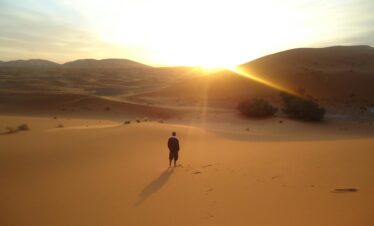 Person walking alone on the desert dunes at sunset