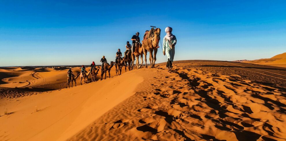 Camel riders journey through golden Sahara sand dunes