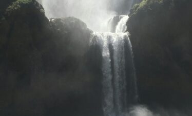 Tall waterfall plunging into a pool with a boat below