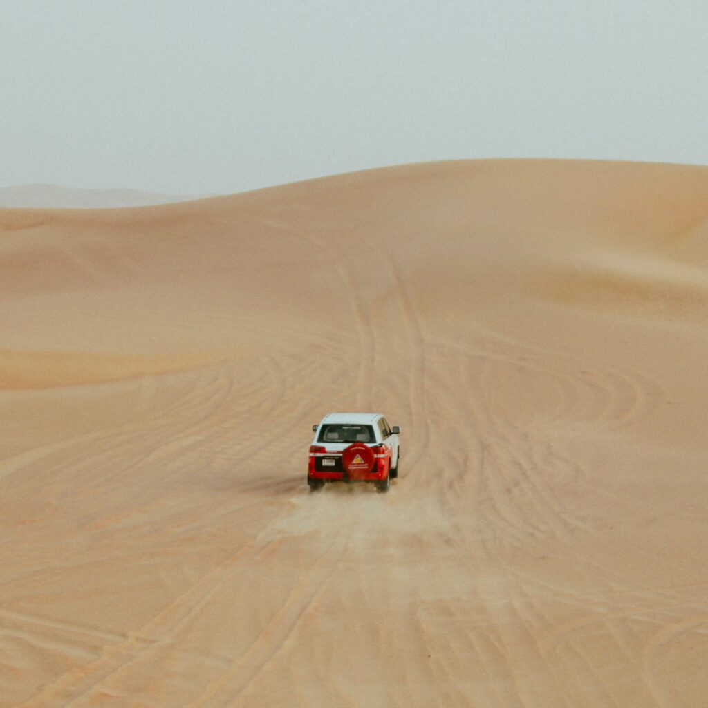 Red rally car driving through Moroccan sand dunes
