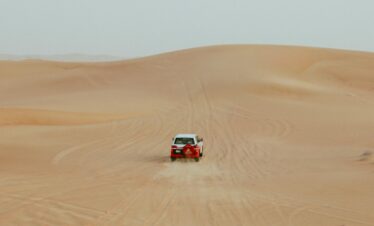 Red rally car driving through Moroccan sand dunes