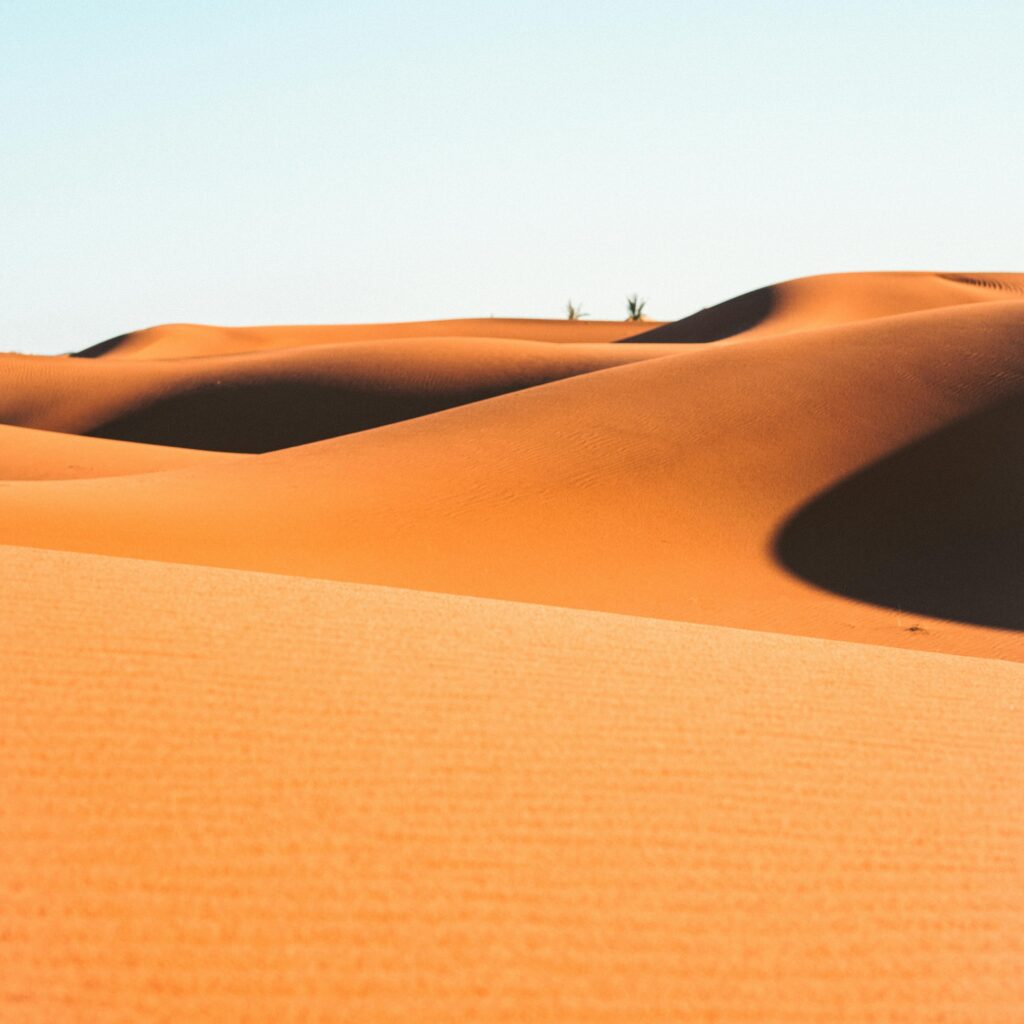 Lone traveler walking across orange Moroccan dunes
