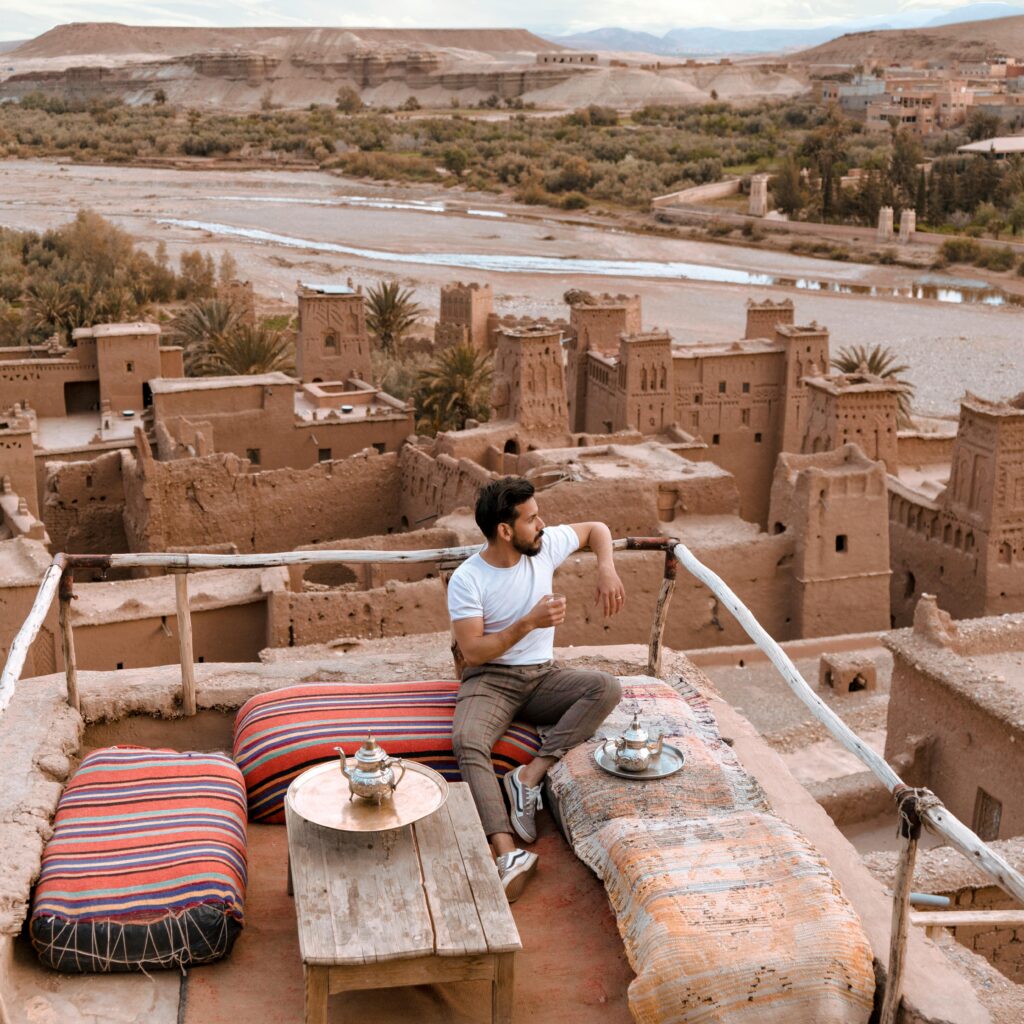 Moroccan man serving tea on a rooftop terrace with mountain views