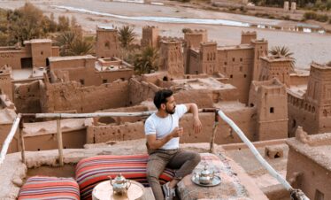 Moroccan man serving tea on a rooftop terrace with mountain views