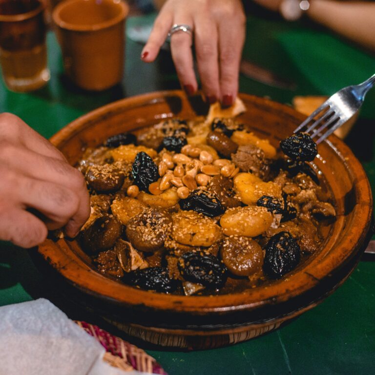 Hands serving meatballs and vegetables from tagine