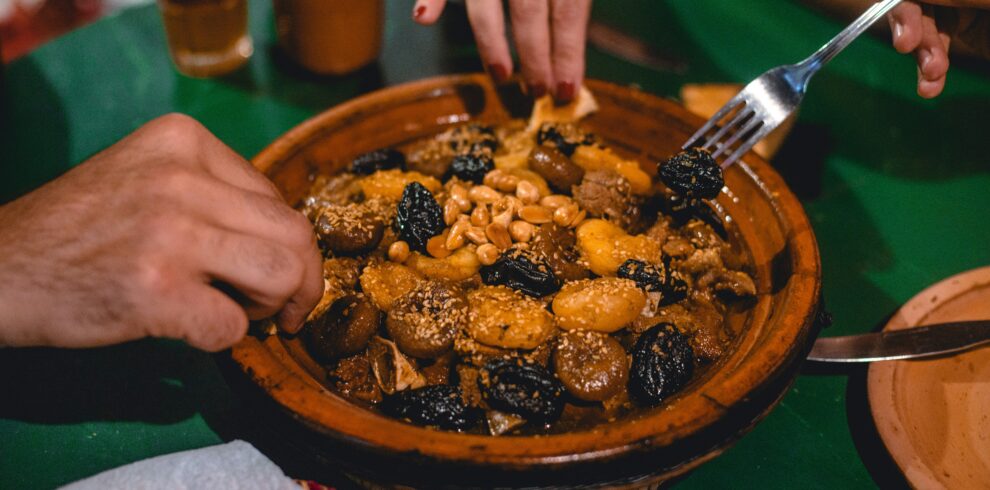 Hands serving meatballs and vegetables from tagine