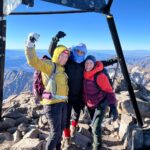 Home - Hayya Morocco Climbers posing with a summit marker in snowy conditions