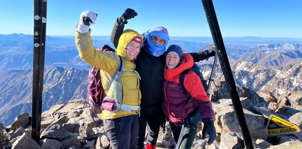 Climbers posing with a summit marker in snowy conditions
