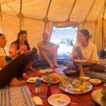Home - Hayya Morocco Tourists sharing traditional Moroccan food inside a tent