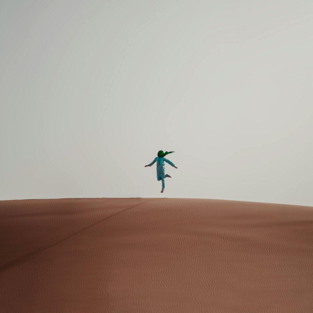 Person jumping on top of a sand dune