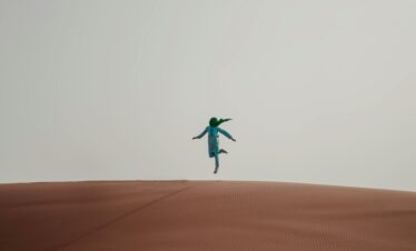 Person jumping on top of a sand dune