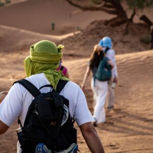 Desert Trekking People walking through desert dunes with a camel
