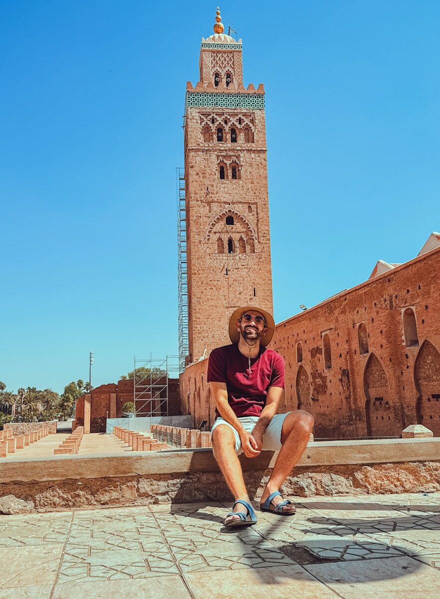 Study Abroad Morocco Man in hat sits near koutoubia mosque in marrakech.