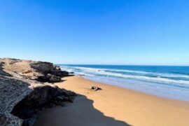 Coastal Road Trip Morocco a sandy beach with rocks and water on a sunny day