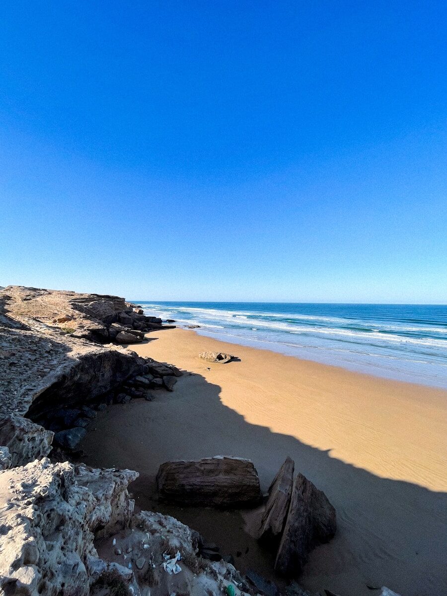 Coastal Road Trip Morocco a sandy beach with rocks and water on a sunny day