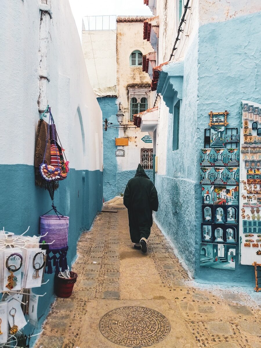Photography person wearing hooded jacket walking on alley between buildings during daytime