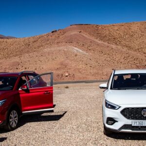 Driving in Morocco Two cars parked in a dry, mountainous landscape.