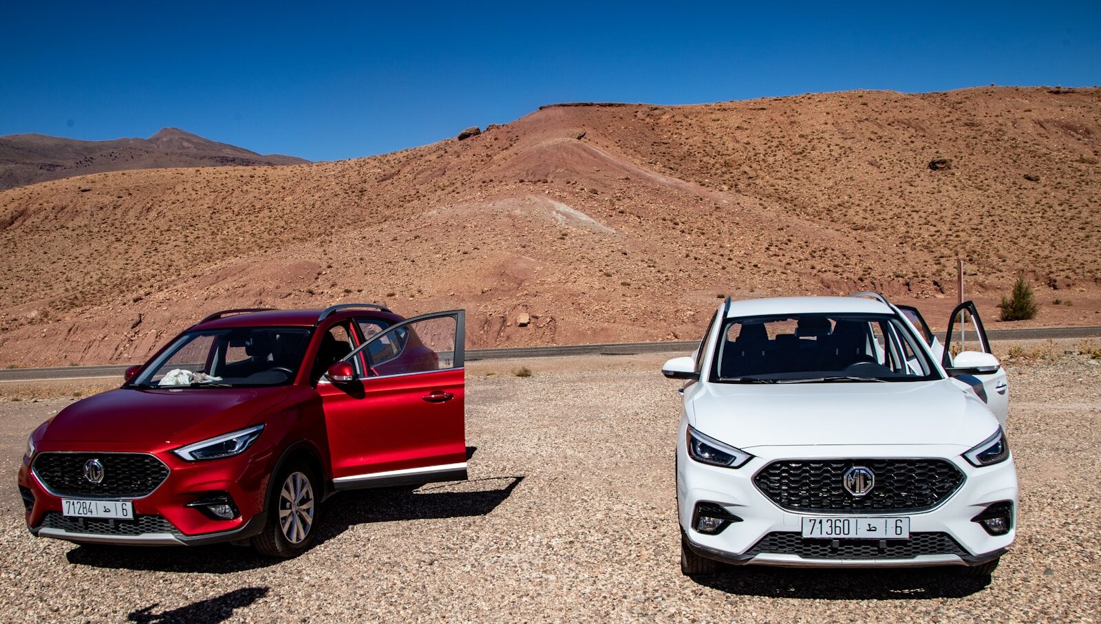 Driving in Morocco Two cars parked in a dry, mountainous landscape.
