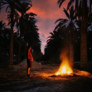 Sahara Photography man in red jacket standing near bonfire during night time