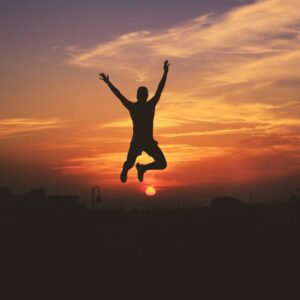 silhouette of man jumping raising both hands during golden hour