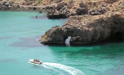 white and red boat on blue sea near brown rock formation during daytime