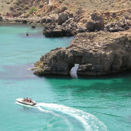 white and red boat on blue sea near brown rock formation during daytime