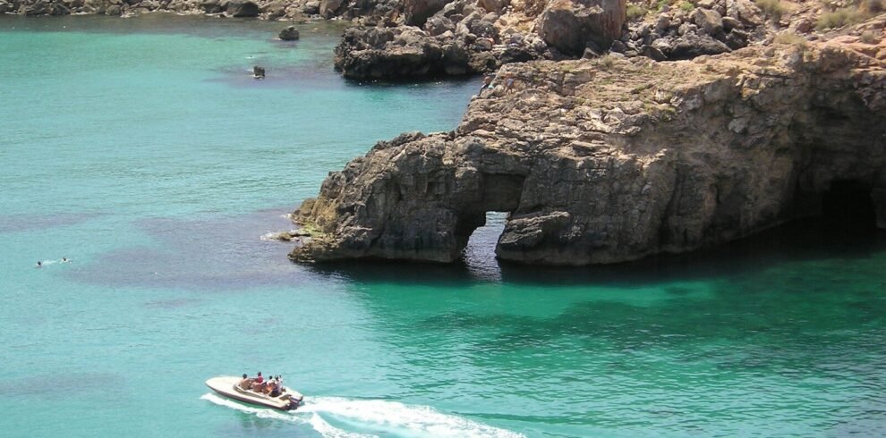 white and red boat on blue sea near brown rock formation during daytime