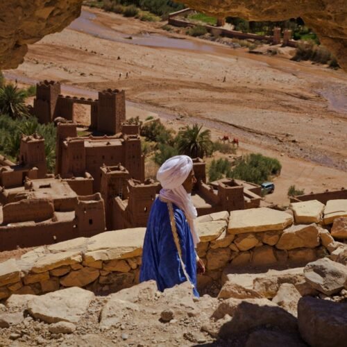 a woman in a blue dress standing in front of a desert village