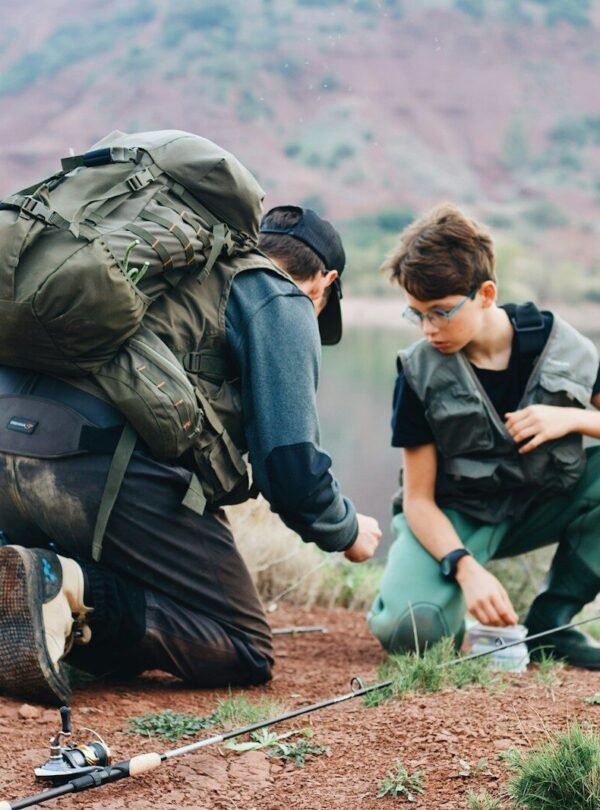 a couple of men with backpacks on a hill with a body of water in the background