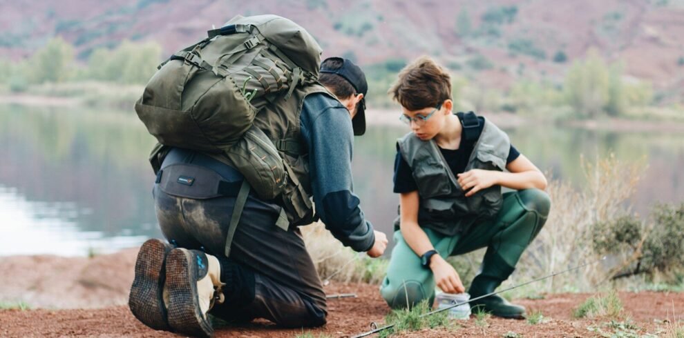 a couple of men with backpacks on a hill with a body of water in the background