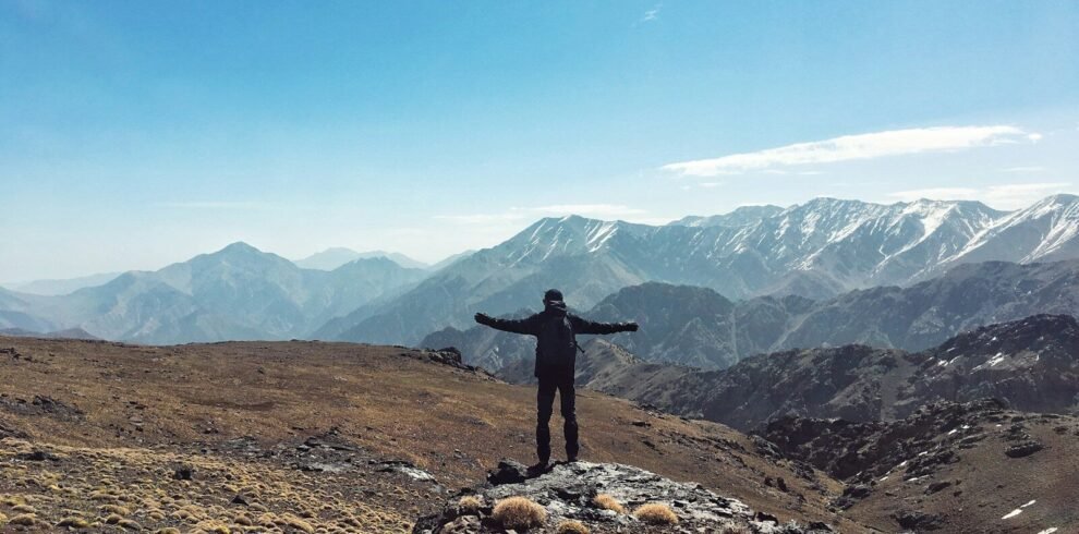 a person standing on a rocky hill with mountains in the background