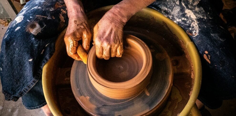 person in blue denim jeans making clay pot