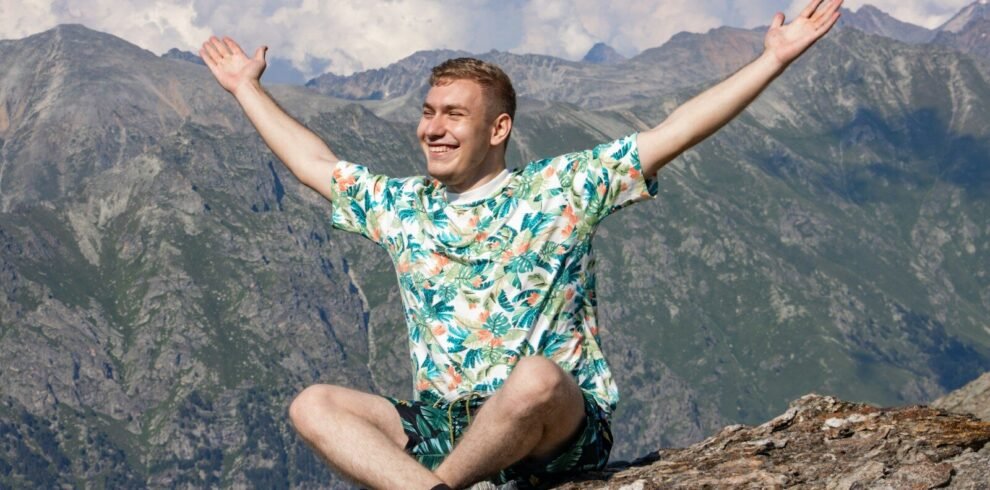 a man sitting on top of a mountain with his arms wide open