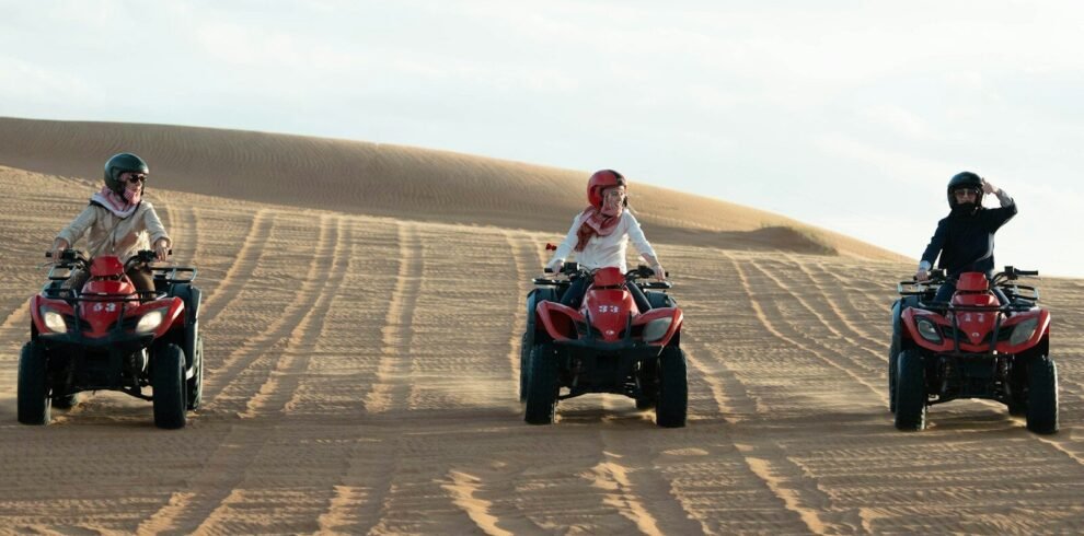 Three people riding atvs on sand dunes