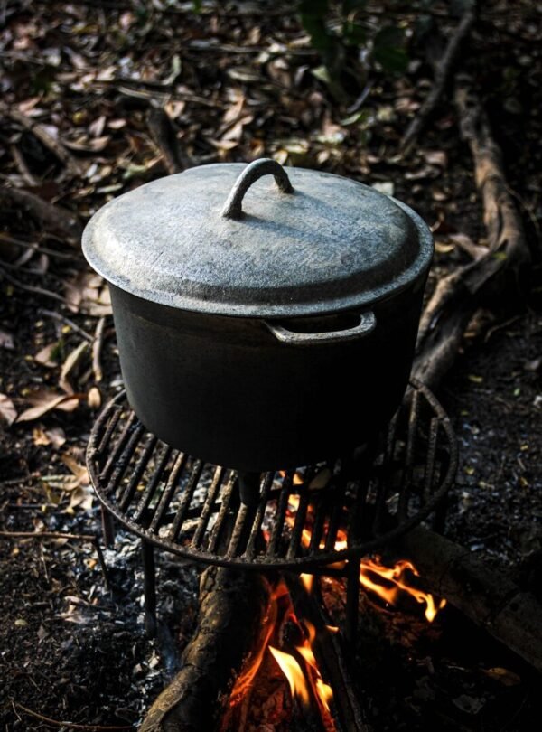 A cast iron pot on a grill over a campfire.