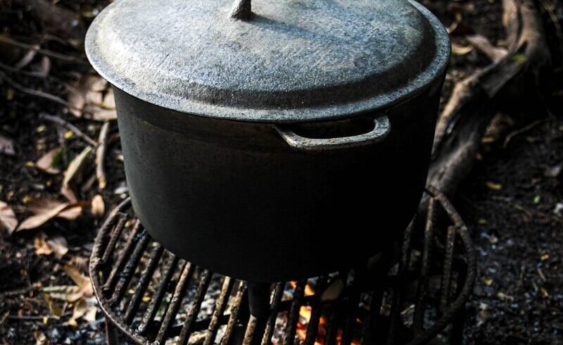 A cast iron pot on a grill over a campfire.