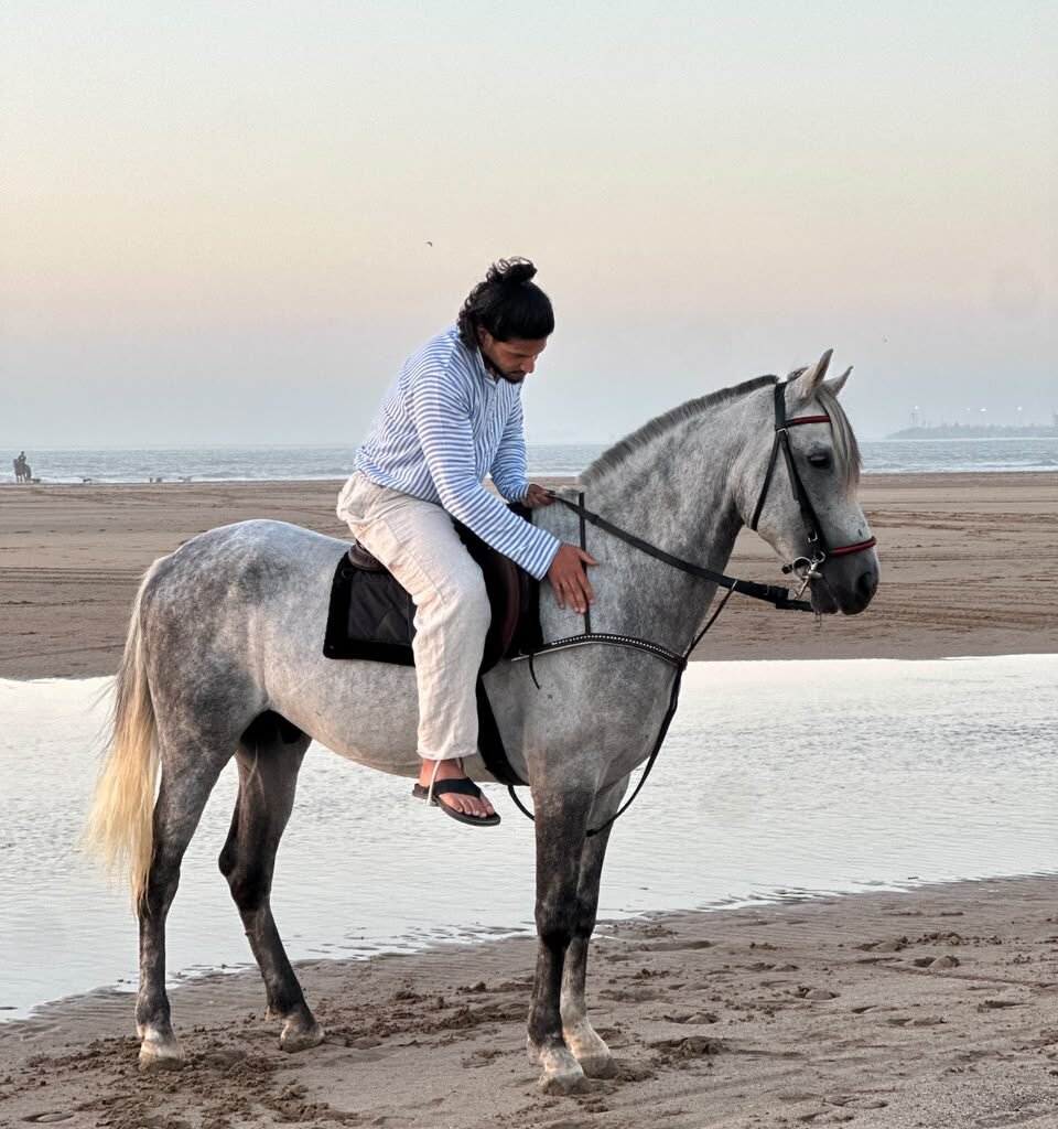 Man riding a white horse along the wet sand shore during sunset in Morocco