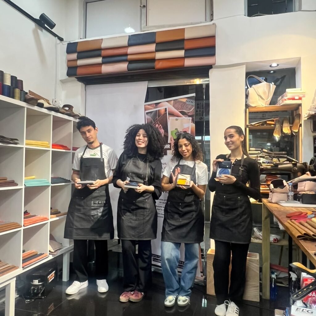 Four workshop participants showing off handcrafted leather items inside an artisan studio