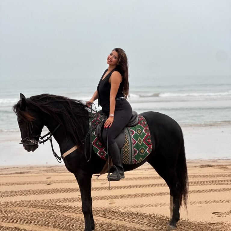 Female traveler riding a black horse along a sandy ocean beach