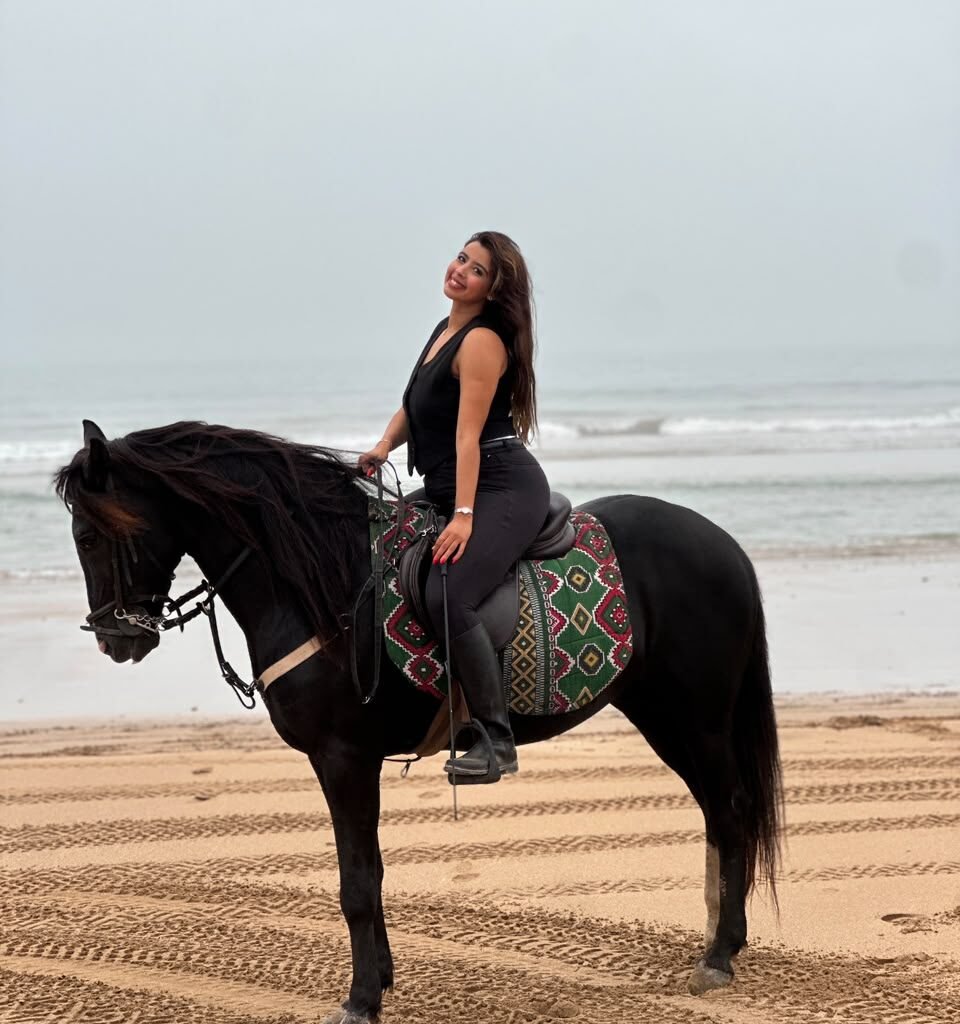 Female traveler riding a black horse along a sandy ocean beach
