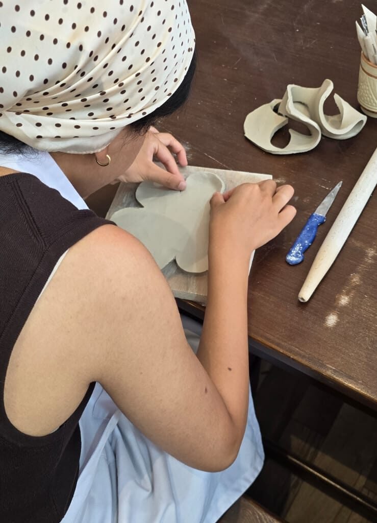 Person shaping clay on a wooden board during a hand-building pottery session