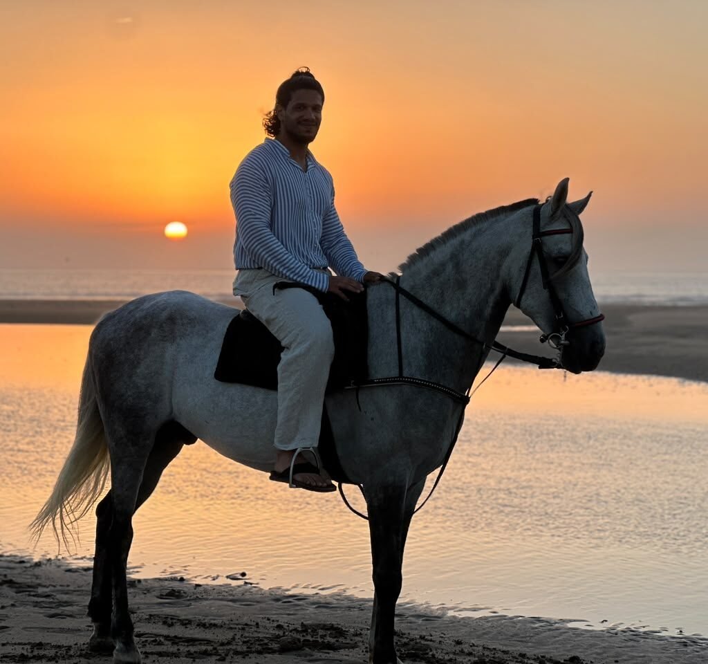 Man riding a white horse on the beach during a vibrant golden hour sunset in Morocco