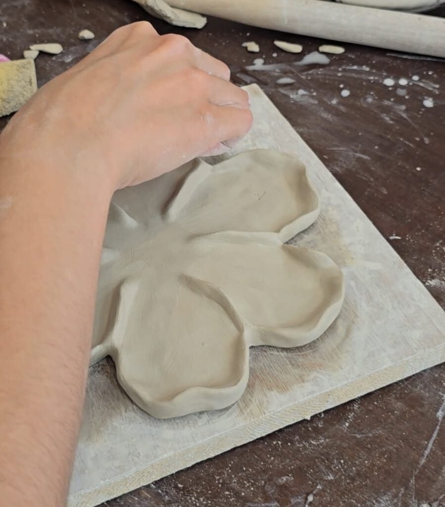 Person smoothing the edges of a newly shaped flower-shaped clay plate