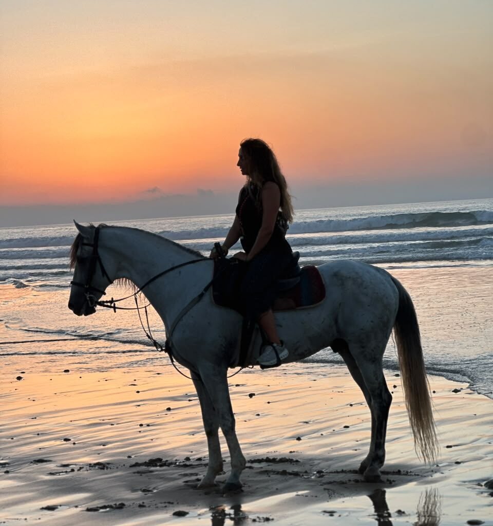 Silhouette of a woman horseback riding a white horse along the ocean shore during sunset in Morocco