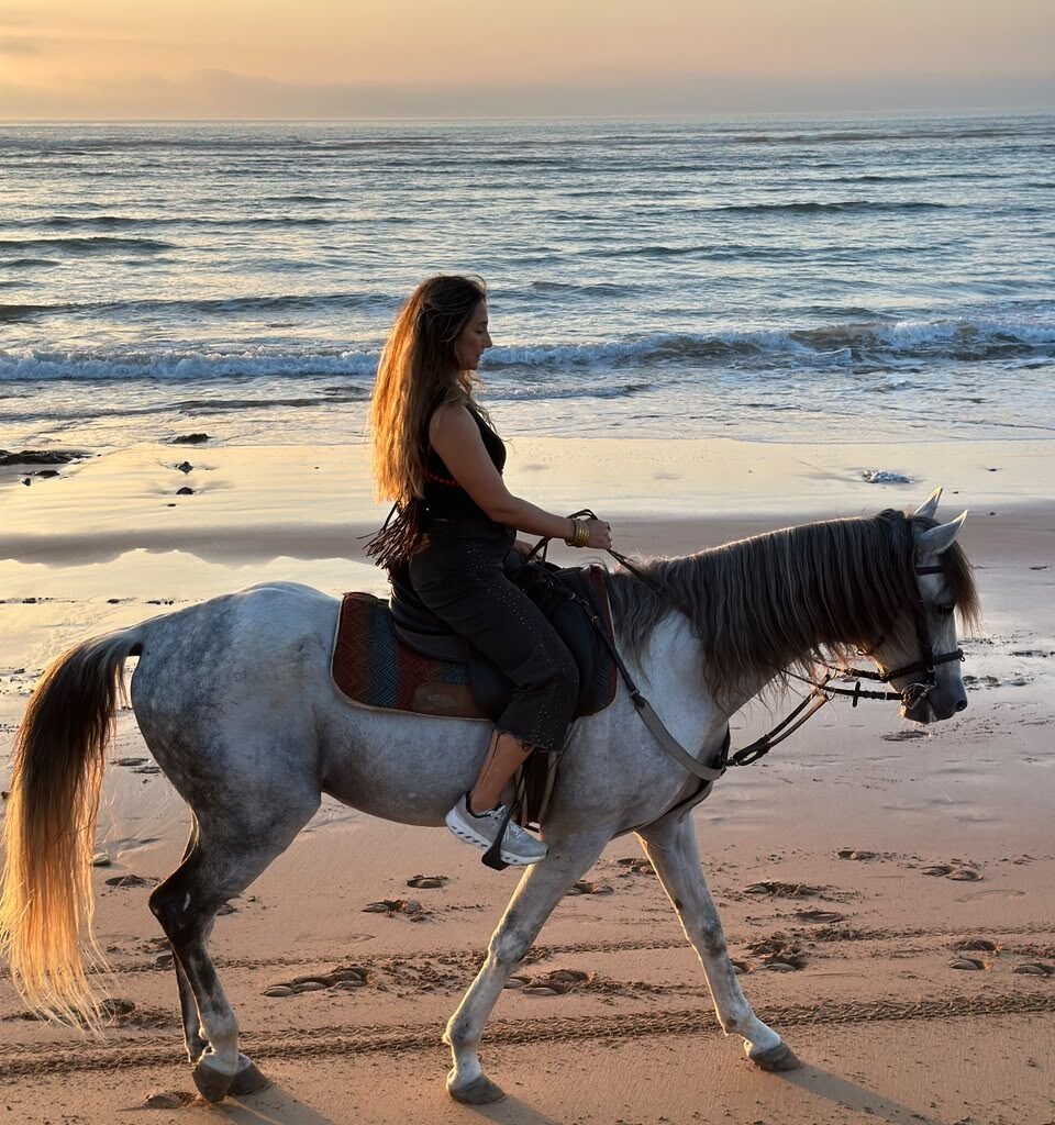 Woman horseback riding a white horse along the wet sand on an Agadir beach