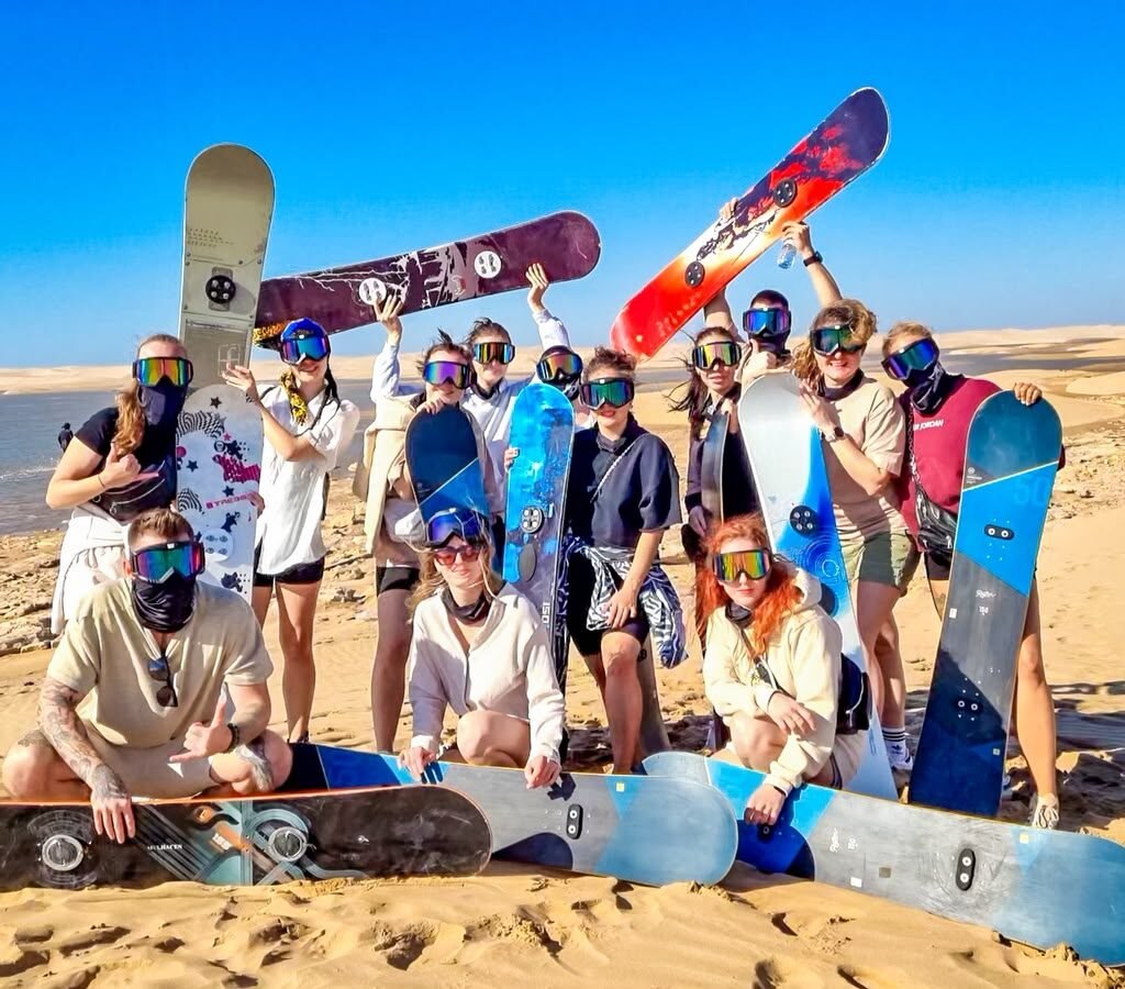 Group of tourists posing with sandboards on coastal desert dunes near the ocean