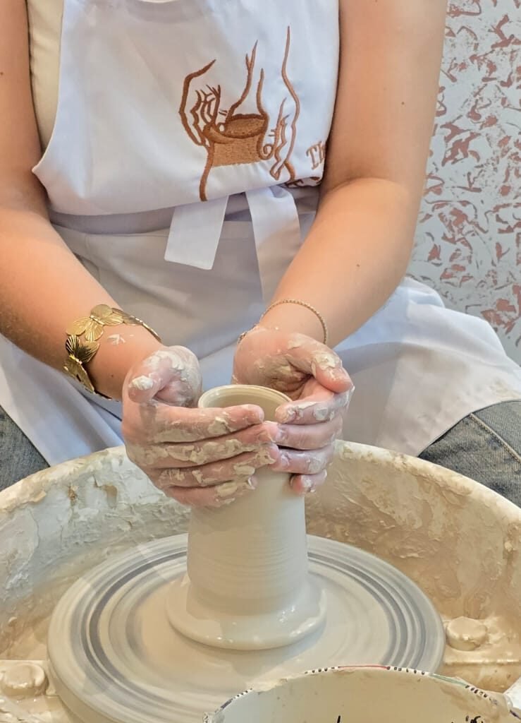 Woman shaping and pulling a clay cylinder on a pottery wheel