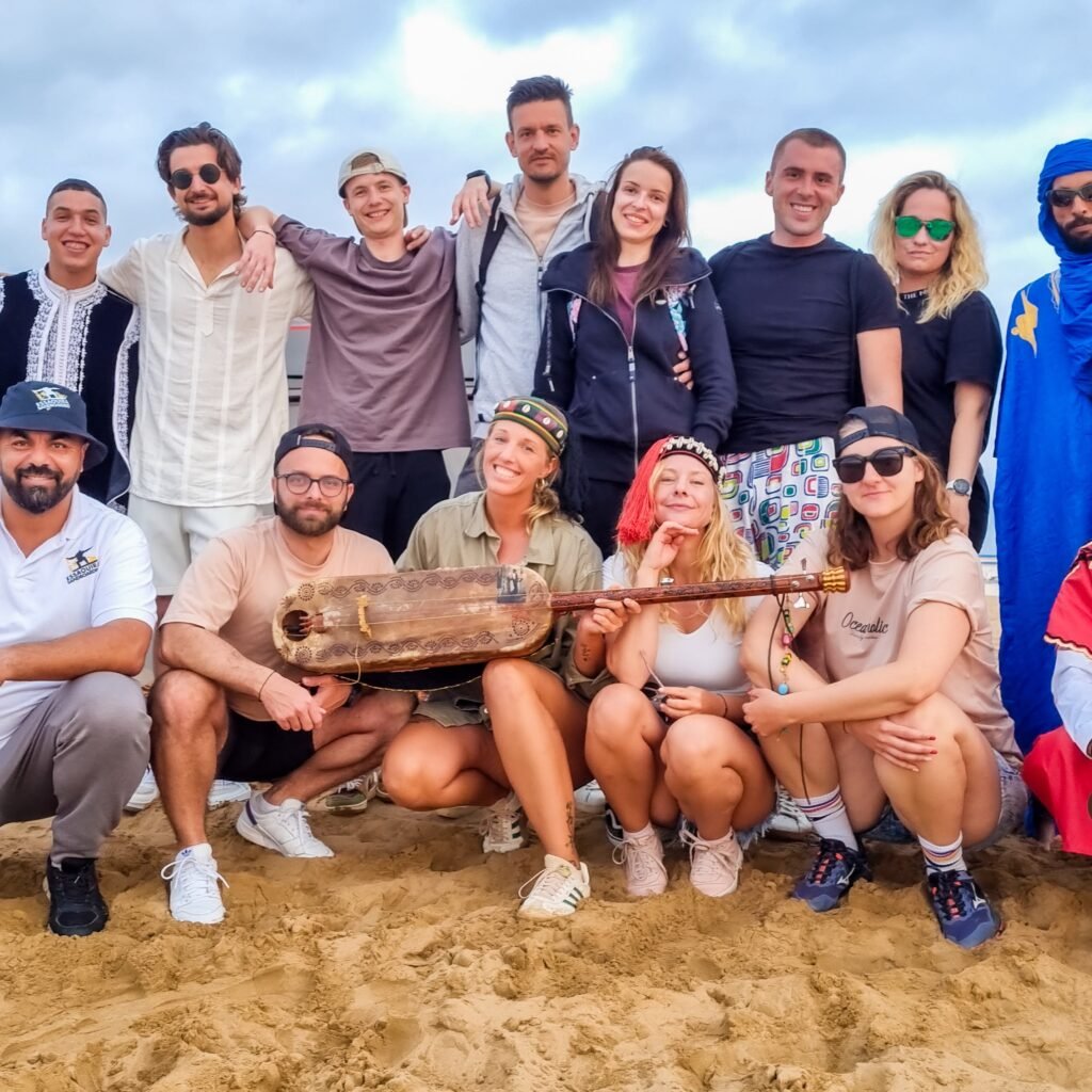 Group of tourists and local guides posing on desert sand with traditional Moroccan musical instruments