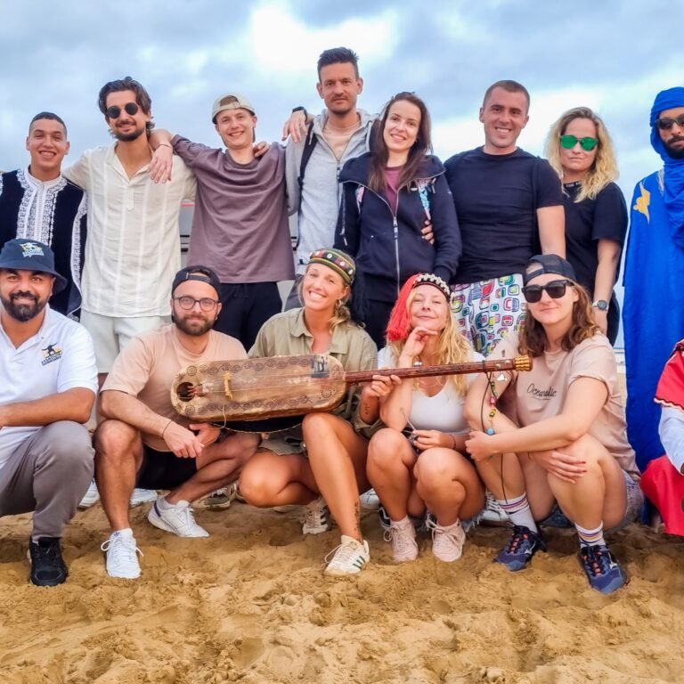 Group of tourists and local guides posing on desert sand with traditional Moroccan musical instruments
