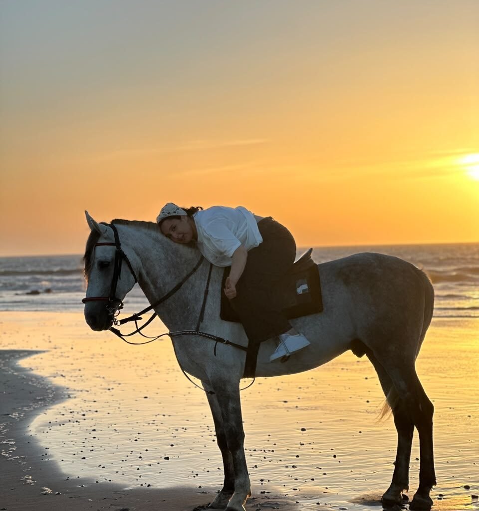 Female traveler leaning lovingly on her white horse's neck at sunset on